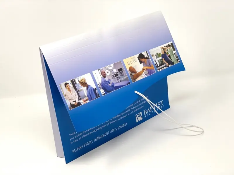 Baptist Health Care folder standing open, the cover printed with a band of care photography