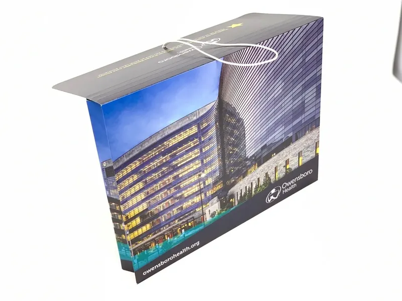 Owensboro Health folder standing closed, the cover printed with a night view of the hospital tower